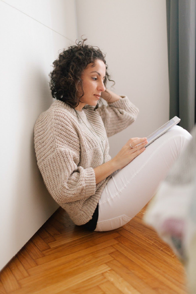 Woman sitting on floor against wall reading a book